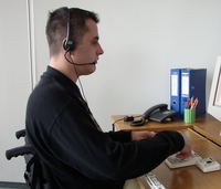 Foto: Junger Mann im Rollstuhl, der mittels Spracheingabe und einer speziellen Tastatur seinen Computer bedient.